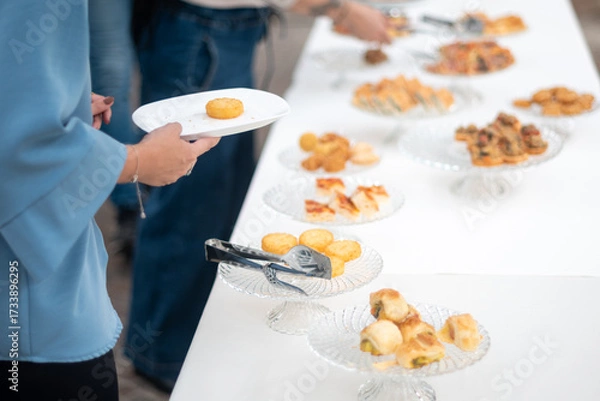 Fototapeta Guests enjoy an elegant private event buffet selection of gourmet appetizers and finger foods served on a long white table during a social gathering