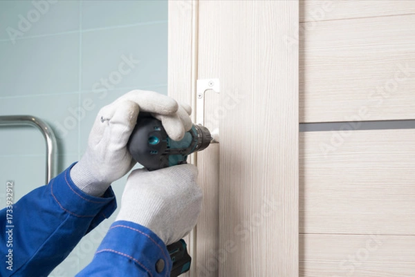 Fototapeta the master installs an interior door by screwing the hinge to the doorway, close-up, master's hands in gloves