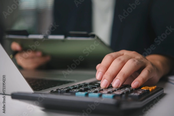 Obraz Accountant hand using calculator business finance, calculating tax, budget planning, financial analysis of documents on clipboard, working at office desk with laptop, bookkeeping and audit concept.