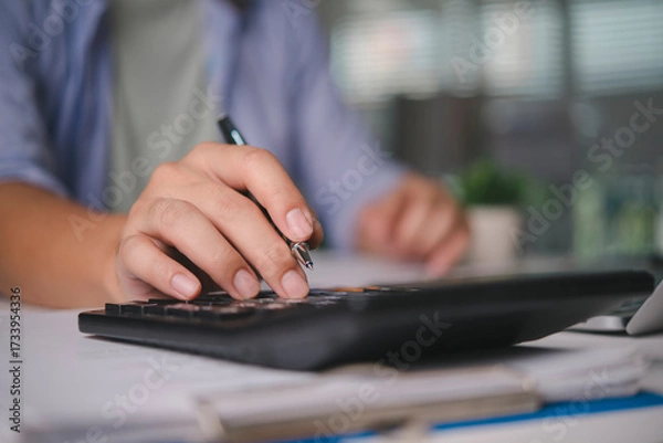 Obraz Accountant calculating finance data on calculator, working on business documents, audit report, money management, tax season, investment analysis, financial planning with paperwork at the office.