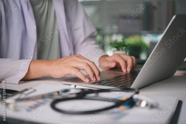 Obraz Male physician using computer for online patient consultation, managing digital health records, medical diagnosis on desk with stethoscope, representing telehealth and modern healthcare services.