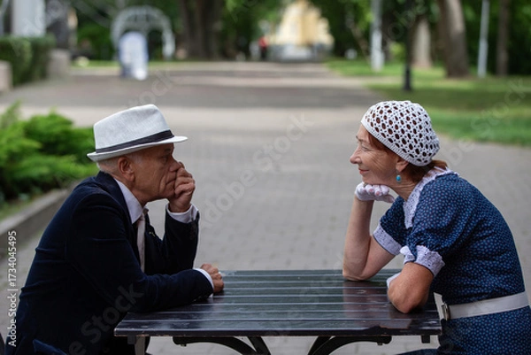 Fototapeta Elderly couple enjoying conversation at a park table during a sunny afternoon in summer