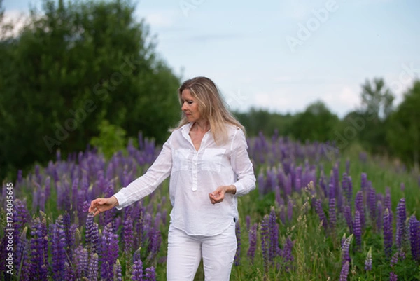 Fototapeta Woman enjoying a stroll through a vibrant purple flower field in summer, surrounded by blooming lupines and greenery