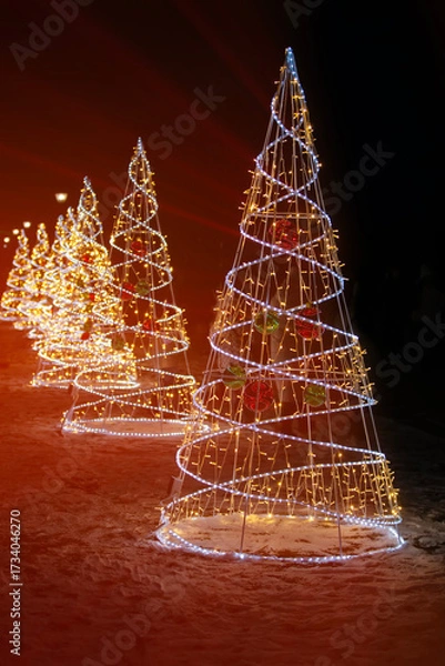 Fototapeta Beautifully illuminated Christmas trees lining a snowy path during the evening celebration