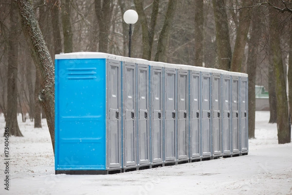 Fototapeta Rows of portable toilets in a snowy park during winter season