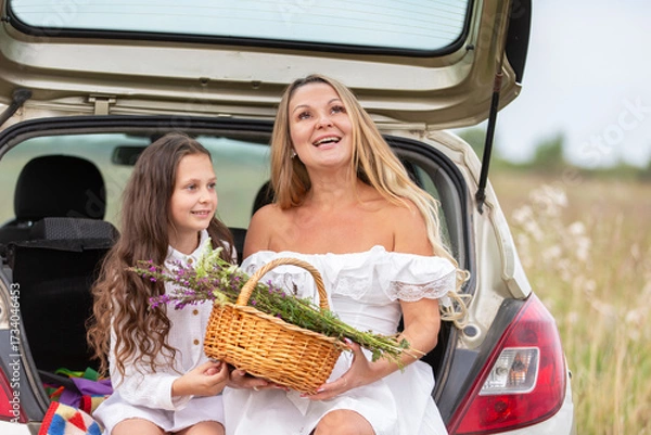 Fototapeta Mother and daughter enjoying a summer day, gathering flowers and sharing smiles in a scenic field