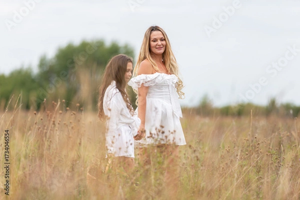 Fototapeta Enjoying a peaceful day in a grassy field with mother and daughter dressed in white attire