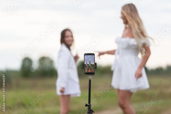 Fototapeta Friends record video in a scenic outdoor setting during a cloudy day with a smartphone on a tripod