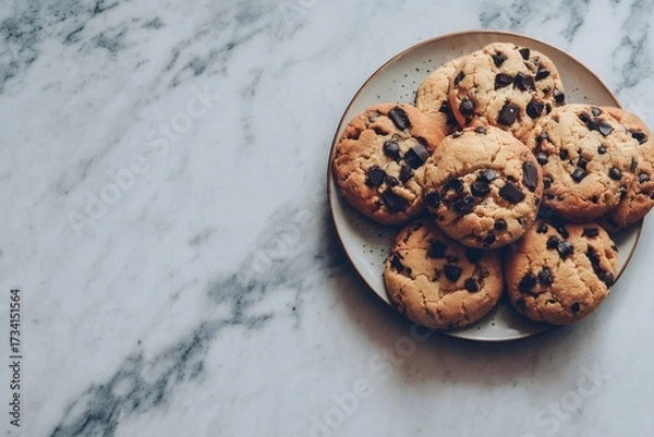 Fototapeta Chocolate chip cookies freshly baked on a ceramic plate, resting on a white marble countertop from an overhead view