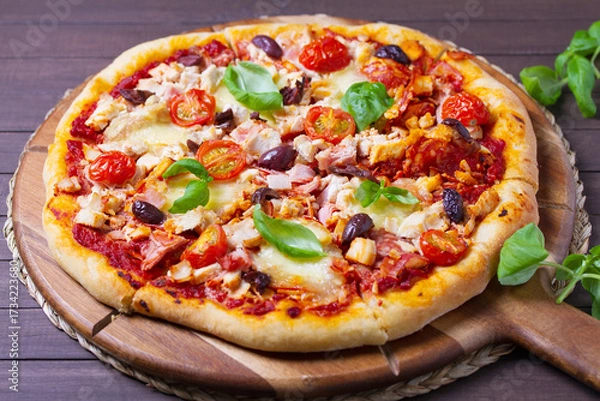 Fototapeta Pizza with melted cheese, crispy crust, topped with olives and basil leaves