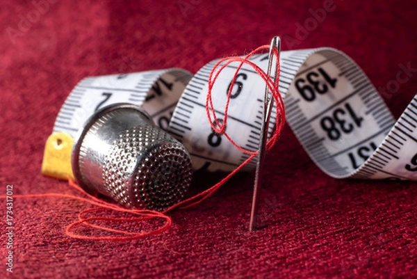 Fototapeta A needle and thread, a tape measure, and a thimble are lying on the fabric. Sewing supplies