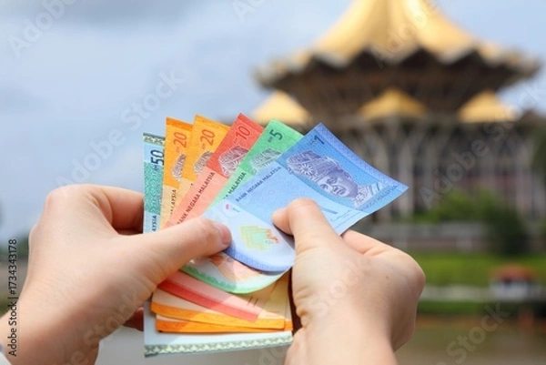 Obraz Hand holding Malaysian ringgit paper money with Kuching city skyline in background.