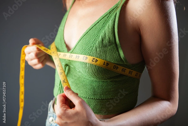 Fototapeta Young woman measuring her waist with a tape measure, close-up