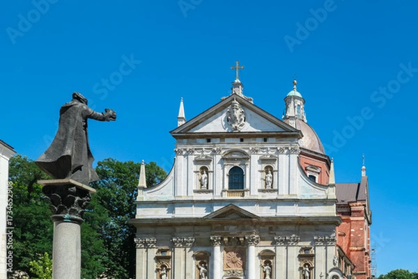 Obraz The magnificent white Baroque facade of the Church of Saints Peter and Paul in Krakow, Poland, gleams under a vibrant blue sky, fronted by statues of the Apostles and a historic stone monument.