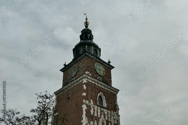 Obraz The historic brick Town Hall Tower with its prominent clock faces stands majestically against a dramatic, overcast sky in Krakow's Old Town, a symbol of the city's rich medieval heritage in Poland.