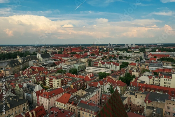 Obraz Wide-angle view of Wroclaw's historic district in Poland, highlighting the dense arrangement of colorful buildings, churches, and urban greenery under a clear sky with soft clouds.