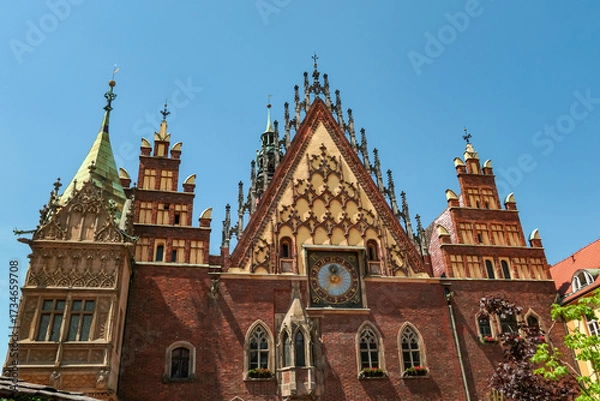 Obraz The decorative front of Wroclaw Town Hall, with its pointed arches and elaborate clock, stands in bright sunlight, highlighting the intricate details of this historic Polish city landmark.