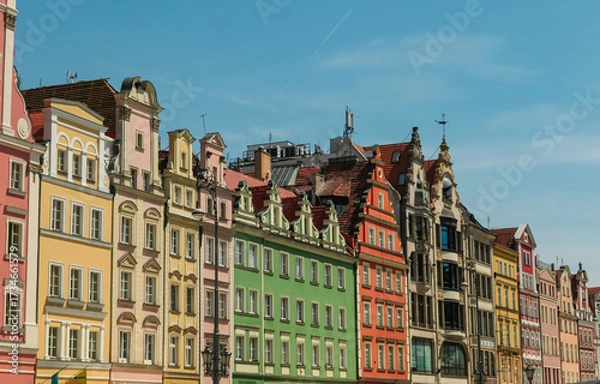 Obraz A vibrant panoramic view of a long row of diverse and brightly colored historic tenement houses lining the Market Square in Wroclaw, Poland, under a clear blue sky with a faint trail.