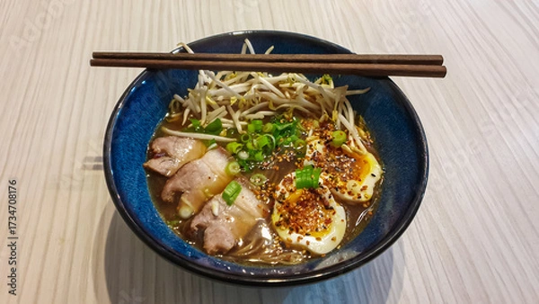 Obraz A steaming bowl of authentic Japanese ramen with pork chashu, soft-boiled egg, and fresh toppings is served on a wooden table, ready for a delicious and comforting meal at home or in a restaurant.