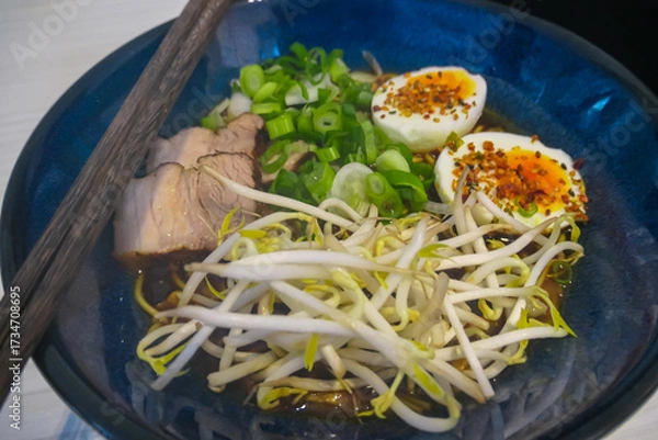 Obraz Delicious bowl of authentic Japanese ramen with rich broth, tender pork, soft-boiled egg, and fresh toppings like bean sprouts and scallions, served in a traditional blue ceramic bowl with chopsticks.