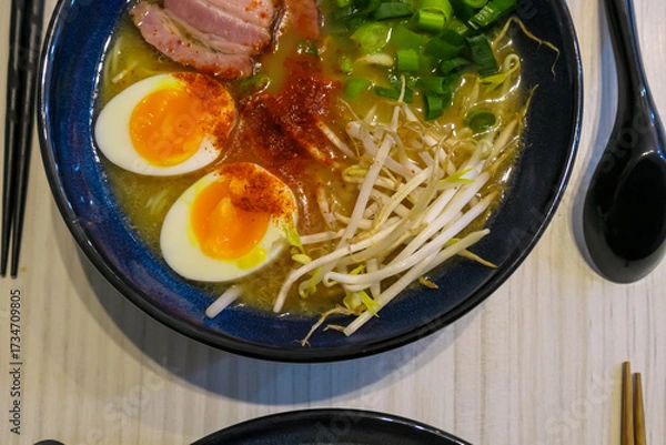 Obraz A steaming bowl of authentic Japanese ramen noodle soup. It features savory pork, a soft-boiled egg, bean sprouts, and green onions, offering a comforting and flavorful meal experience.
