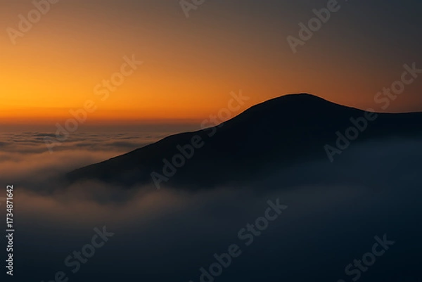 Obraz Mountain peak silhouette above a sea of clouds at sunset.