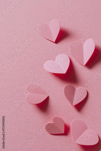 Fototapeta Pink paper hearts scattered across a textured pink surface, creating a whimsical, loving, and visually appealing arrangement.
