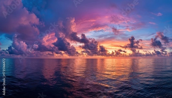 Fototapeta The sun sinks into the calm ocean, painting the sky in glowing hues of orange, pink, and purple with clouds reflecting the evening light.