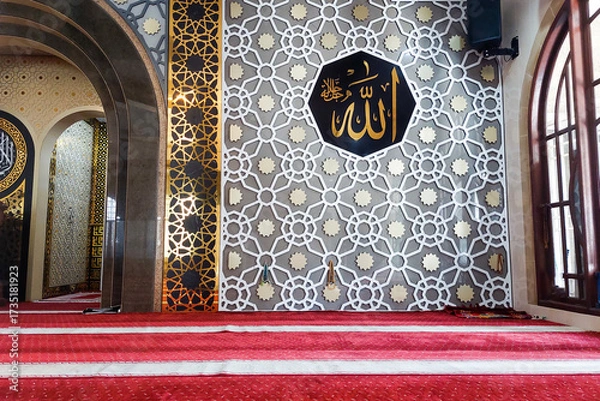 Fototapeta An interior view of a mosque featuring a beautifully decorated wall with Islamic geometric patterns, golden calligraphy of Allah’s name.or.