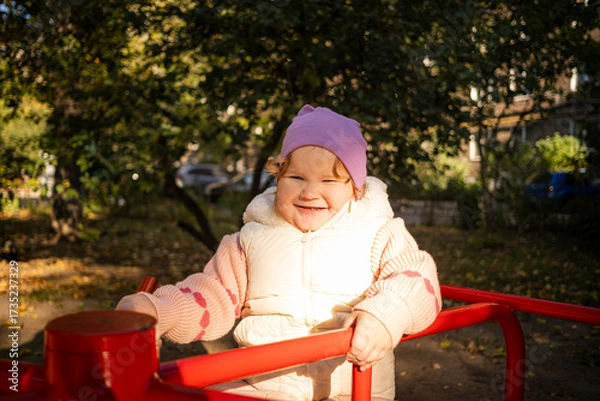 Fototapeta A cheerful child rides on a vibrant carousel in a lively park surrounded by colorful autumn leaves. The sun shines brightly as joyful laughter fills the air.