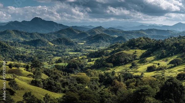 Fototapeta Lush green hills and mountains under a cloudy sky creating a scenic landscape view from above