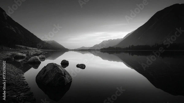 Fototapeta Black and white landscape featuring a tranquil lake with mountains and rocks in the foreground