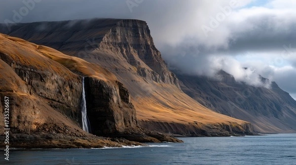 Fototapeta Stunning waterfall cascading down rocky cliffs under a cloudy sky in a scenic coastal landscape