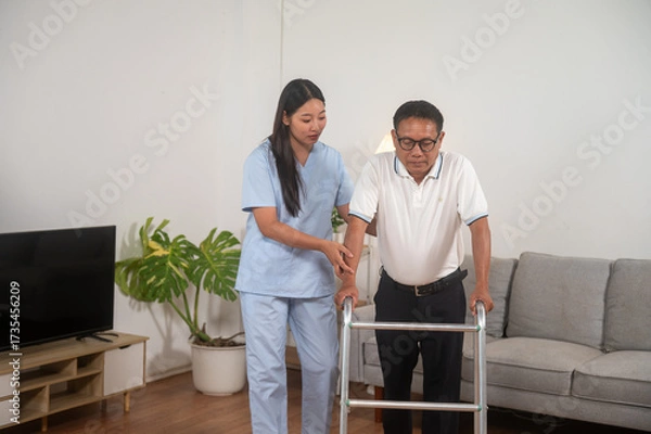 Fototapeta Supportive Stroll: A healthcare worker assists an elderly individual using a walker indoors, portraying care and rehabilitation with a focus on mobility and wellness.