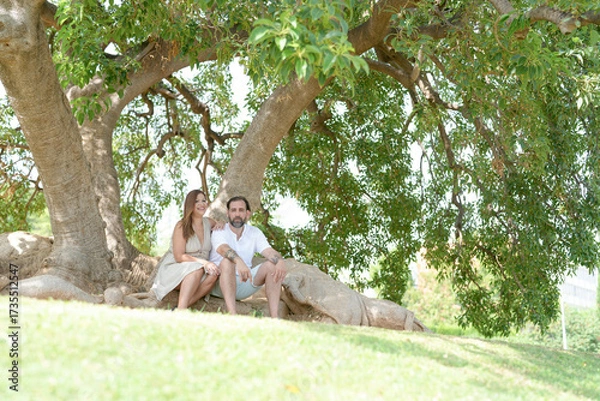 Fototapeta A couple is sitting under a tree, enjoying each other's company. Scene is peaceful and romantic