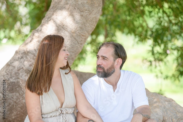 Fototapeta A man and a woman are sitting on a tree branch, smiling at each other. Scene is happy and relaxed
