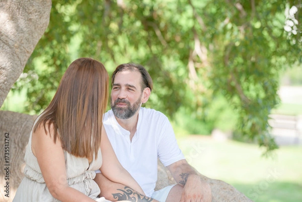 Fototapeta A man and woman are sitting on a tree branch, smiling at each other. Scene is happy and relaxed