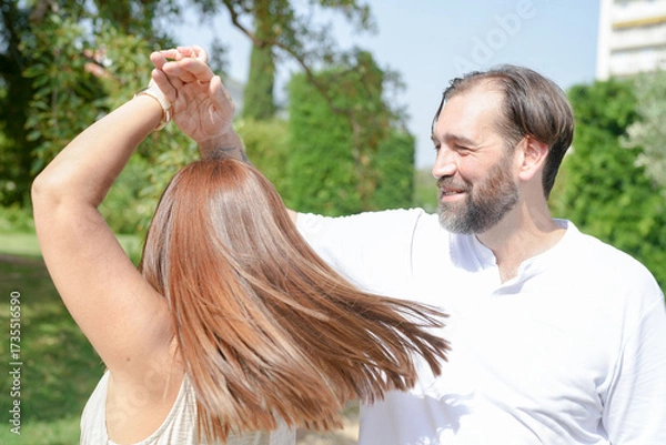 Fototapeta A man and a woman are dancing together in a park. The man is smiling and the woman is laughing