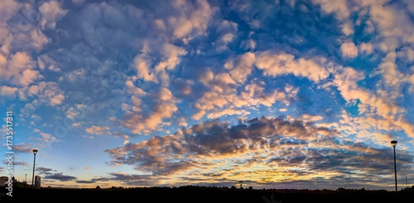Fototapeta Cumulus sunset clouds with sun setting down. Magical curls of orange clouds lined up like a fabulous pattern on the evening blue sky. Yellow and red accents, a play of warm and cold tones.