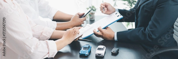 Fototapeta Panorama view of business meeting with car loan agreement, dealer showing calculator to customers at office desk with vehicle model and key, concept of auto finance, leasing or insurance. car loan.