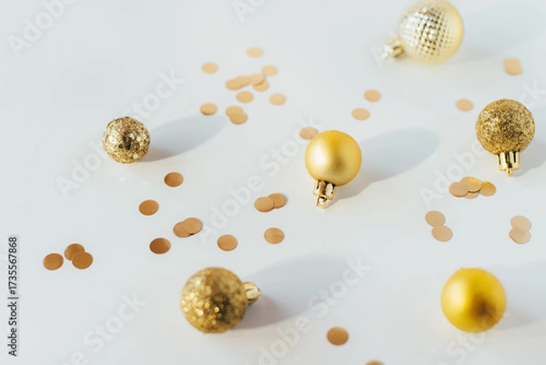 Fototapeta Golden Christmas balls and confetti on a white table in bright light