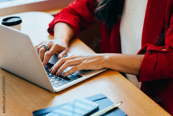 Fototapeta Woman typing on a laptop while wearing a red blazer at a desk