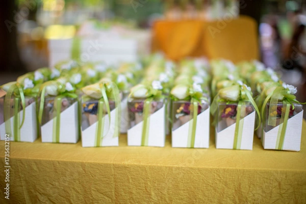 Obraz Elegant wedding favors bomboniere arranged on a table at a reception. Each box is decorated with ribbons and flowers, containing traditional sugared almonds.