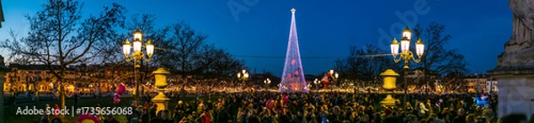 Obraz A large crowd gathers in Piazza delle Erbe, Padua, for a Christmas celebration. The square is illuminated by a modern light tree and festive decorations at dusk.