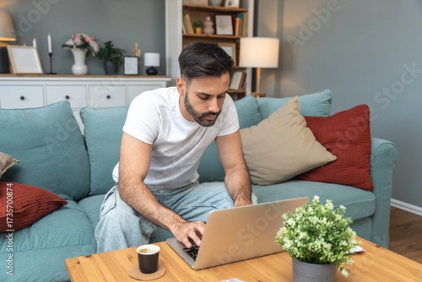 Fototapeta Young university student, freelancer business man, working at home on laptop computer, testing new innovative technology and online internet tools while sitting in home office.