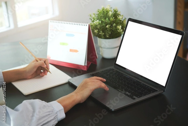 Fototapeta Businesspeople working on laptop with blank screen taking notes with calendar on desk office