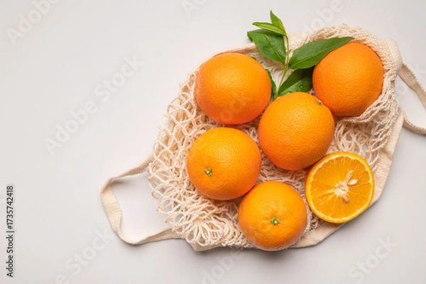 Fototapeta Eco-friendly thread bag for shopping, buying food, fruits, vegetables. Ripe juicy oranges in cotton string bag on gray background top view flat lay. Zero waste, plastic free concept. Citrus fruits
