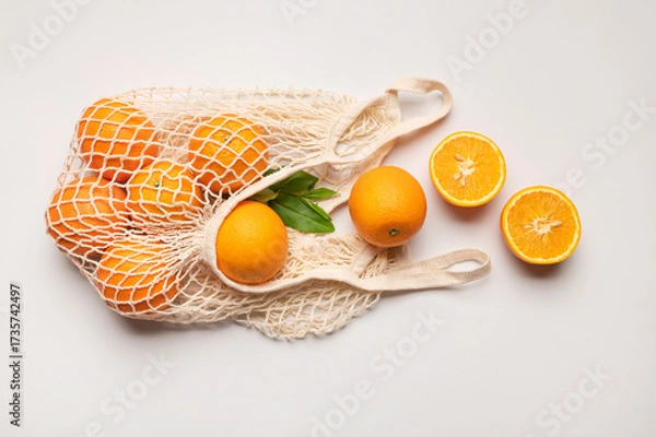 Fototapeta Eco-friendly thread bag for shopping, buying food, fruits, vegetables. Ripe juicy oranges in cotton string bag on gray background top view flat lay. Zero waste, plastic free concept. Citrus fruits