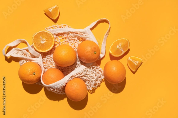 Fototapeta Eco-friendly thread bag for shopping, buying food, fruits, vegetables. Ripe juicy oranges in cotton string bag on yellow background top view flat lay. Zero waste, plastic free concept. Citrus fruits