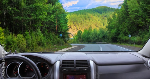 Fototapeta View from the car of a beautiful winding road in the forest with mountains